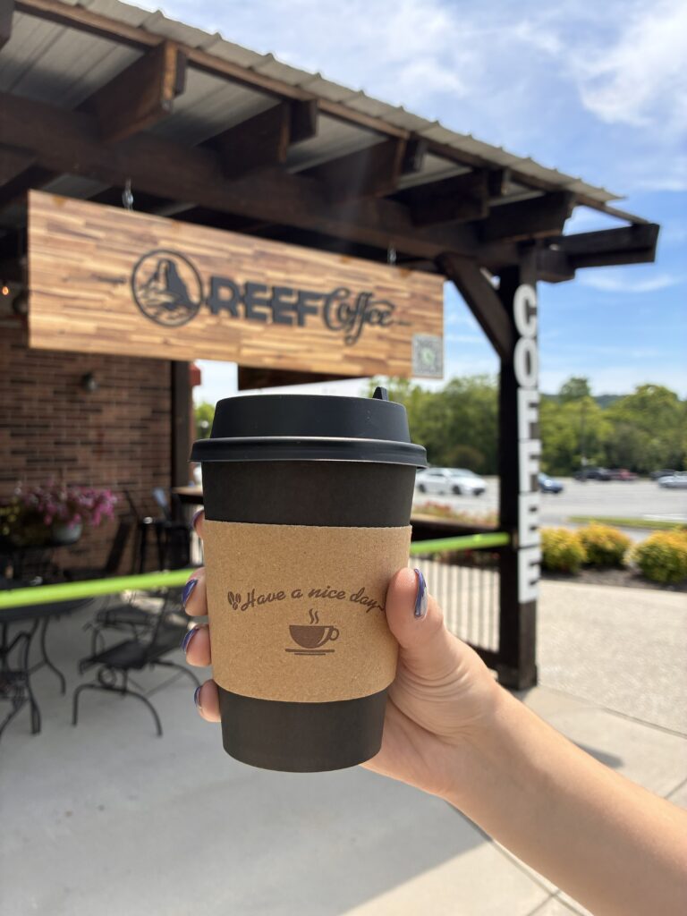 Reef Coffee  exterior sign and person holding hot coffee cup