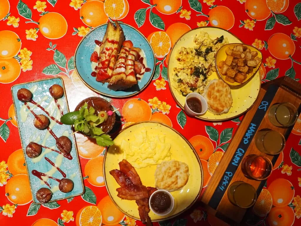 Flying Biscuit Cafe Brunch spread on table. Beignets, bacon, eggs, french toast, scramble, mimosa
