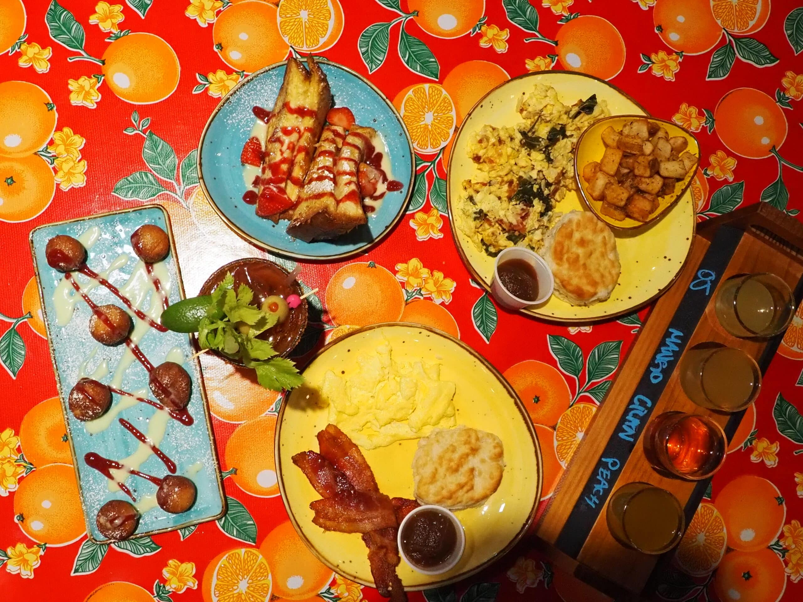 Flying Biscuit Cafe Brunch spread on table. Beignets, bacon, eggs, french toast, scramble, mimosa