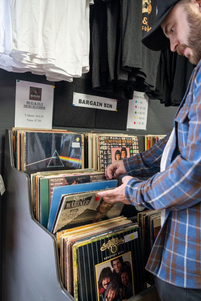 Man flipping through a bin of vinyl records labeled "bargain bin"