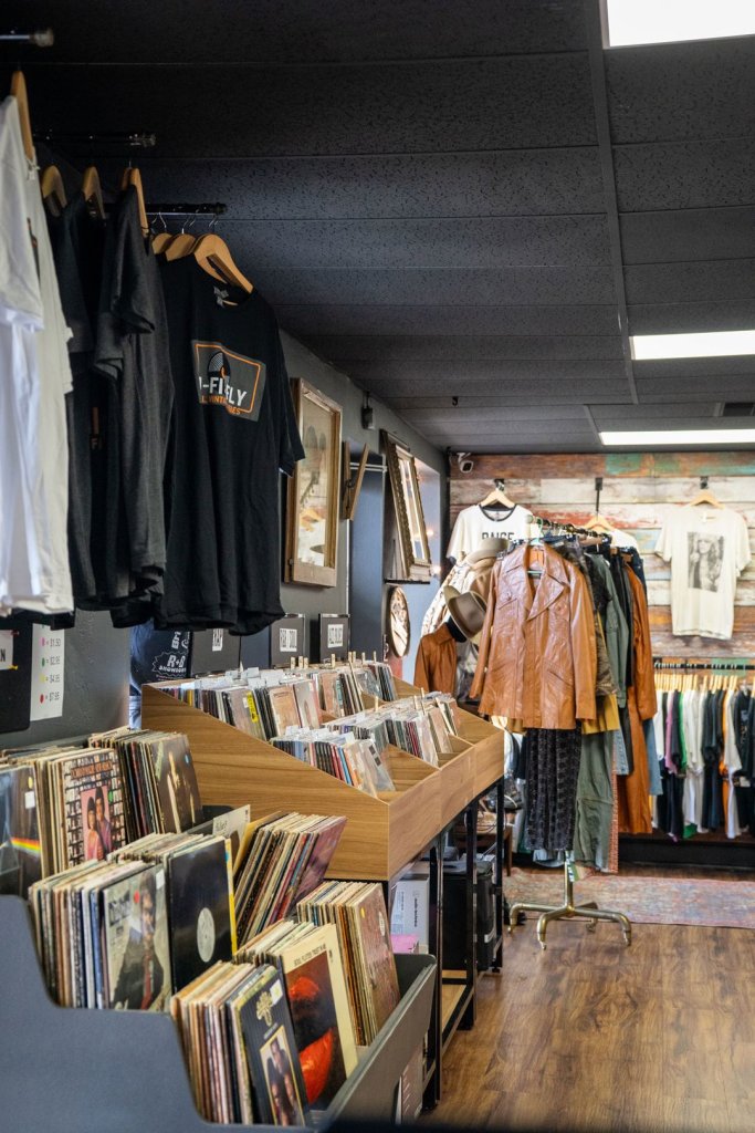 a few racks of vinyl records and several clothing racks of vintage clothing and t-shirts that say "Hi-Fi and Fly"
