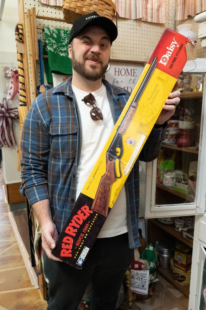 Man holding up a Red Ryder B-B gun still in its box.