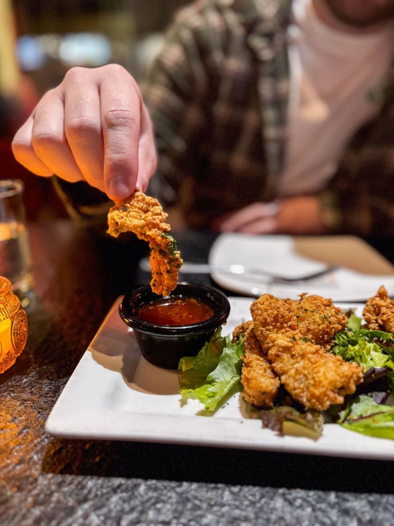 hand dipping a fried chicken strip into a sauce at Season's Innovative Bar & Grille