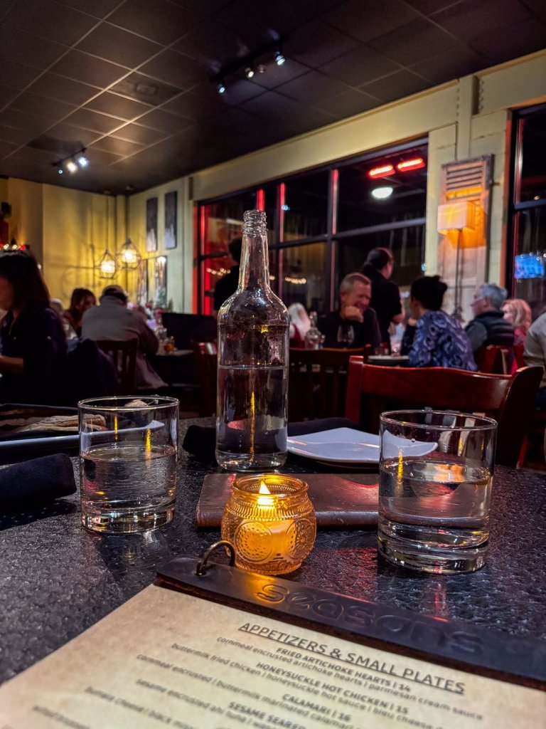 Table at Seasons with glasses of water, a lit candle, and people dining in the background