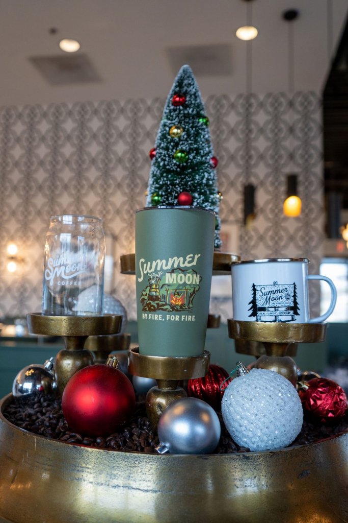 summer moon merch including a glass, a campfire mug, and an insulated tumbler in front of holiday decor